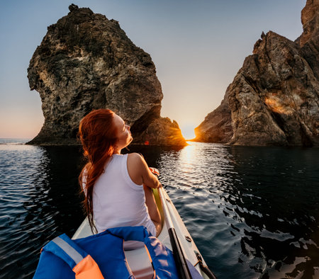 Kayaking woman sunset adventure as a red haired female explorer sits in a boat between massive sea cliffs during golden hourの写真素材