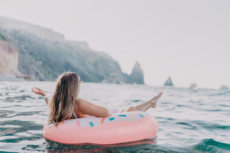 Woman, ocean, donut. Young woman relaxing on a fun donut inflatable ring in the calm sea near scenic...