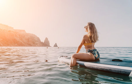 Woman Paddleboard Ocean - A woman relaxes on a paddleboard in the ocean with mountains in the...