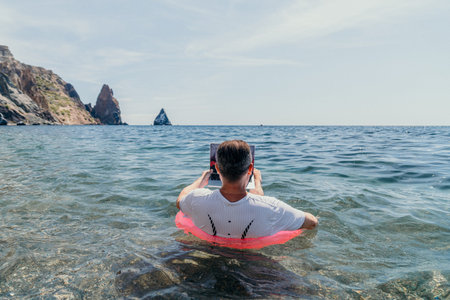 Laptop ocean vacation showing a man using a computer while floating in an inner tube in the sea for...