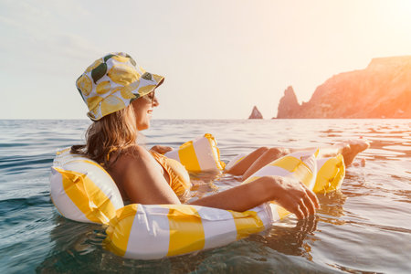 Woman Beach Float Relaxation - Young woman in a yellow bikini relaxing on a yellow and white float in the ocean on a sunny day.の写真素材