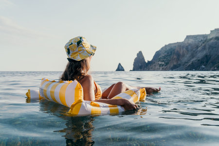 Woman, Beach, Relaxation: A woman in a hat floats on an inflatable raft in the ocean, enjoying the...