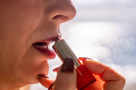 Lipstick makeup application close up of woman applying red lipstick on lips outdoors by the sea