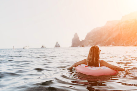 Woman, floating, sea. Young woman relaxing on inflatable ring in ocean water, enjoying scenic sunset...