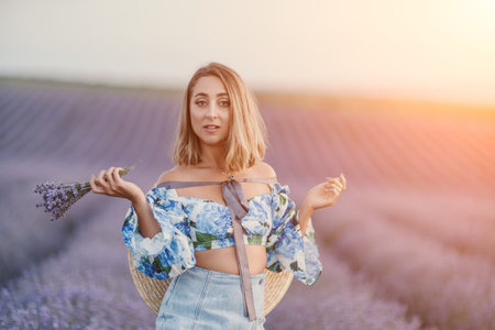 Lavender woman field stands in a blooming purple flower meadow holding a bouquet during a beautiful sunsetの写真素材