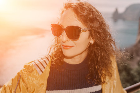 Woman sunset ocean happy traveler in yellow jacket wearing sunglasses enjoys the view overlooking a calm coastal bayの写真素材