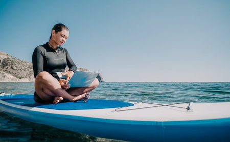 Woman Laptop Paddleboard Ocean - Working Remotely on a Stand Up Paddleboard in the Ocean on a Sunny...
