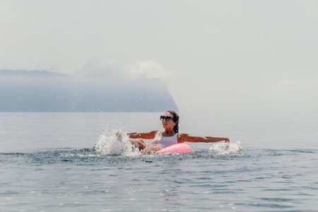Woman splashing ocean happy young female on a pink inflatable ring enjoys summer vacation while...