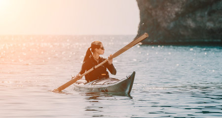 Kayaking Woman Ocean Sunset - A woman kayaks in a small boat on the ocean with a large rock...