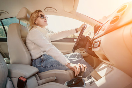 Woman Driving Car Interior Sunlight - A woman wearing sunglasses sits in the drivers seat of a car,...