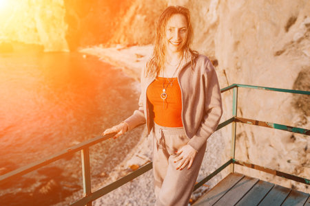 Woman coastline sunset smiling woman in casual wear standing on a cliffside deck overlooking a rocky...