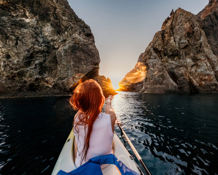 Kayaking sunset adventure redhead woman sits in a kayak between massive rocky cliffs at sunset expressing a sense of peace during solo travelの写真素材