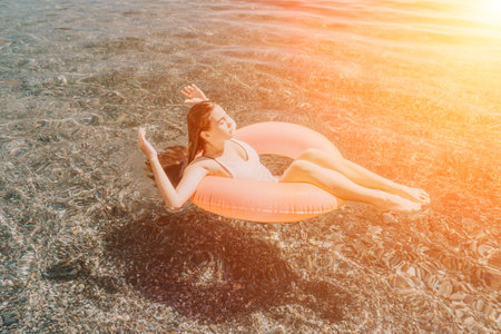 Woman floating tube relaxing on an inflatable ring in the crystal clear sea water under the warm...