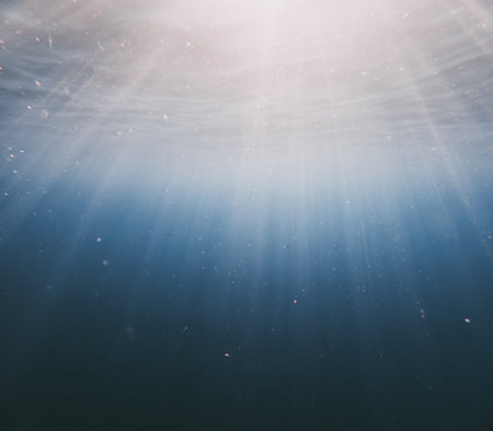 Underwater light rays pierce through clear ocean water illuminating floating particles and deep blue depths