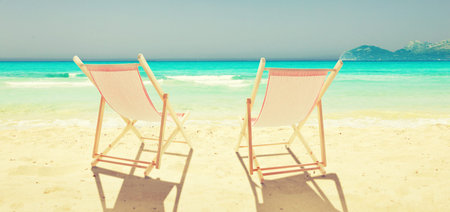 Wooden deck chairs on sandy beach near sea. Holiday background.