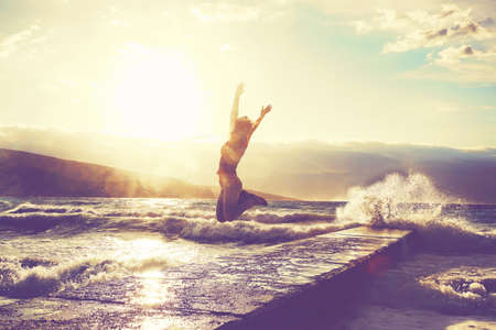 Feeling of freedom concept. Woman jump on pier facing to the sea with big waves.の写真素材