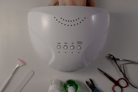 Hand in a lamp for drying gel polish on nails on a light background on the table. In a beauty salon,...