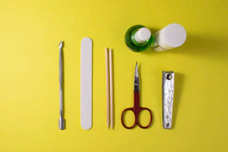 Tools for manicure on a yellow background, top view. A nail file, scissors, wooden cuticle sticks, nail oil on a yellow background, top view.の写真素材