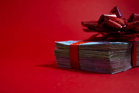 Bundles of new design banknotes drain on a red background including . Money concept. Bundle of money with a red bow. A gift in the form of money.の写真素材