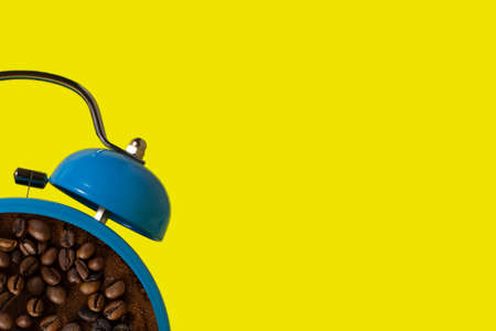 Blue alarm clock with empty coffee inside. Hot coffee retro alarm clock on a yellow background. Breakfast time concept. Minimalistic style.の写真素材