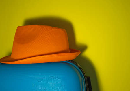 Orange Sun Hat Close-up on a Blue Suitcase on a Yellow Background. Summer Travel Concept. Summer time.の写真素材
