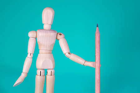 Cheerful Wooden Doll on a Blue Background with a Pencil for Drawing or a Letter with Empty Space for Text. Standing Wooden Man. Wooden Puppet on a Blue Background. Concept of Education and School.の写真素材