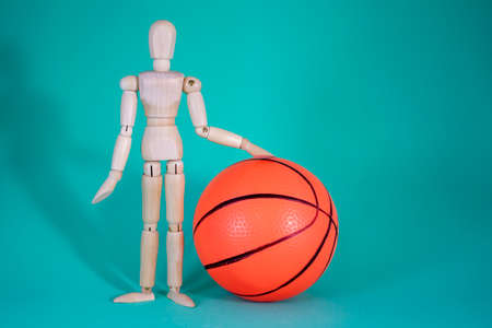 Wood Man and Basketball. Cheerful Wooden Doll on a Blue Background with a Ball for the Game and with an Empty Space for the Text. Game and sport concept.の写真素材