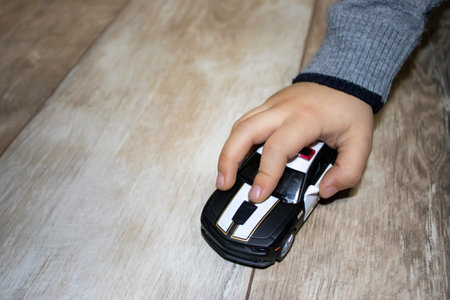 The boy plays at home on a light floor. Black car in the hands on a pastel background. Detail in the...