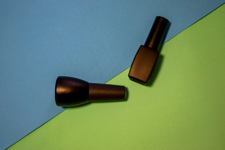 Black Bottles of Nail Polish on a Colorful Table. Bright and Shiny Nail Polish Bottles on Blue and...