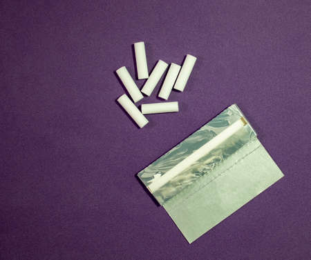 Dry Tobacco on Rolling Paper and Filters on a Purple Background. Finely Cut Tobacco and Smoking Filters for Rolling Cigarettes. Health Concepts and their Environment.の写真素材