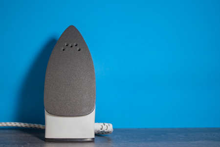 New Green Iron on the Wooden Table. Iron Irons linen. Modern Device For The Care Of Linen And Clothes Near The Blue Wall. Cozy House, Laundry and Ironing. Front View with Copy Space.の写真素材