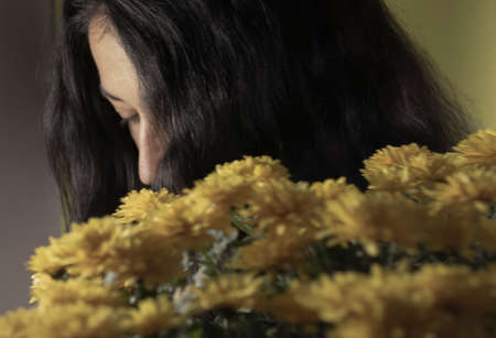A Woman Looks Down in the Background of a Bouquet of Yellow Chrysanthemums. Happy Woman Received a Bouquet of Flowers from a Beloved Person. Side View of Attractive Woman with Bouquet of Flowers.の写真素材