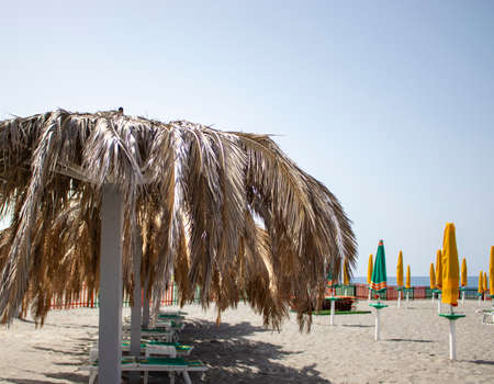 Chairs and an umbrella on the beach made of natural materials. Beach umbrellas with palm leaves. Vacation on the beach in Italy. vacation concept.の写真素材