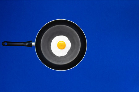 Frying Pan with Fried Egg on a Blue Background. The Concept of Cooking a Dish with an Egg, Frying an...