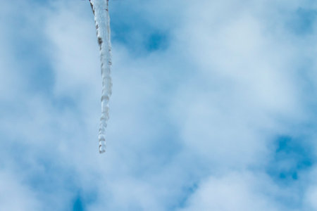 Icicle on the Roof Against the Blue Sky with Clouds. Lonely Icicle. Icicles Hang From the Edge of...
