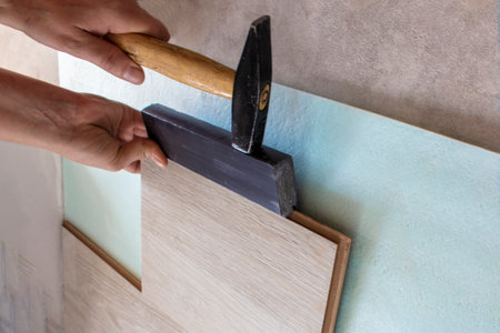 Close-up of a hand with a rubber mallet laying a light wood laminate in the living room. Repair, improvement of the house and office with their own hands. worker. Laying process.の写真素材