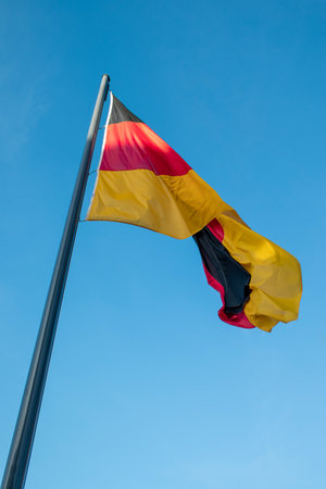 German flag on a flagpole. Waving German flag and blue sky.の写真素材