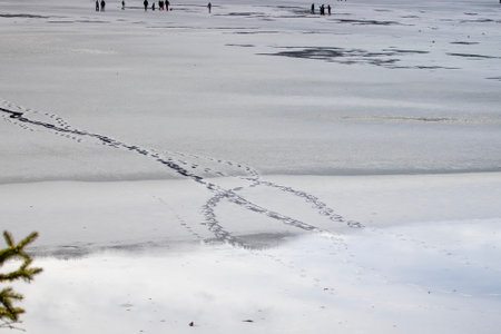 Footprints on Frozen Lake With Distant Figures Enjoying Winter Activities in a Serene Landscapeの写真素材