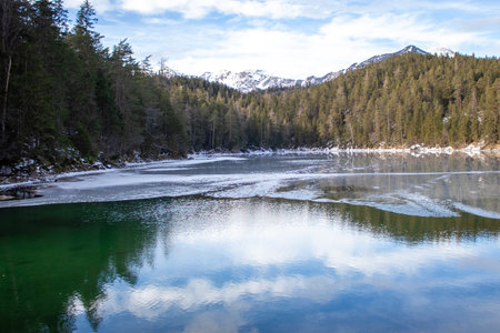 Tranquil Lake Reflecting Mountains Under a Clear Sky With Patches of Snowの写真素材