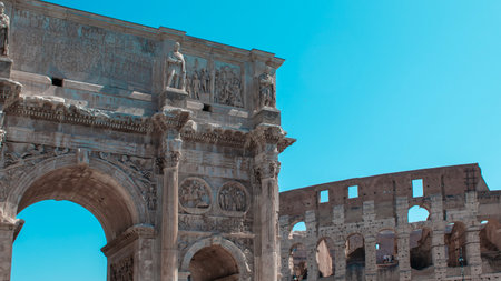 Visitors admire the intricate carvings of the Arch of Constantine while the imposing Colosseum stands proudly beside it. The bright blue sky enhances the ancient feel of the location.の写真素材