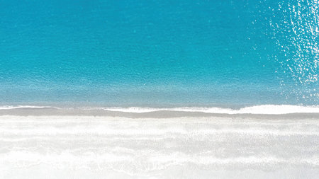 A serene view captures the clear blue ocean gently lapping against a smooth sandy beach. The sun...
