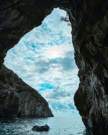 A stunning view captured through a natural rocky archway, revealing a tranquil sea and a partly cloudy sky. The scene showcases the beauty of the coastline and nature's formations. San Nicola Arcella, Calabria, Italy.の写真素材