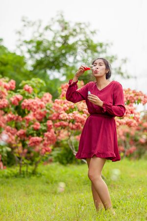 Portrait of beautiful young asian woman with Carmen red dress blowing bubble in the parkの写真素材