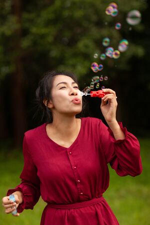 Portrait of beautiful young asian woman with Carmen red dress blowing bubble in the parkの写真素材