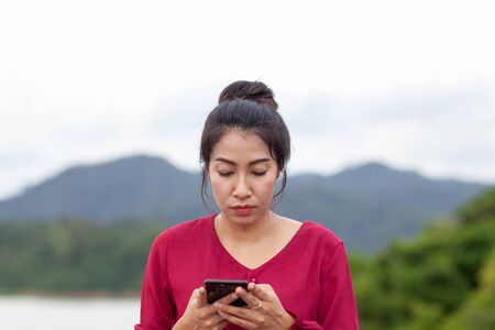 Portrait of beautiful young asian woman with Carmen red dress reading messages on her smartphoneの写真素材