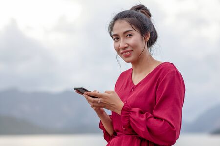 Portrait of beautiful young asian woman with Carmen red dress reading messages on her smartphone and smilingの写真素材