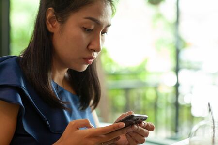 Portrait of beautiful young asian woman reading messages on her smartphone in coffee shopの写真素材