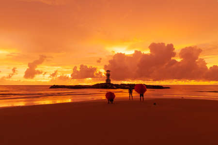 On a rainy day Tourists open umbrellas to watch Beautiful scenery at sunset at a lighthouse in Khao Lak, Phang Nga, Thailand.の写真素材