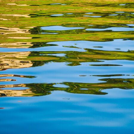 Colorful patterns of blue, brown and green are seen in reflections in the water of a lakeの写真素材