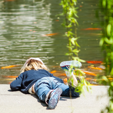 SHANGHAI, CHINA - April 12, 2011 : European girl in blue is playing with the carp fish in the pond.のeditorial素材